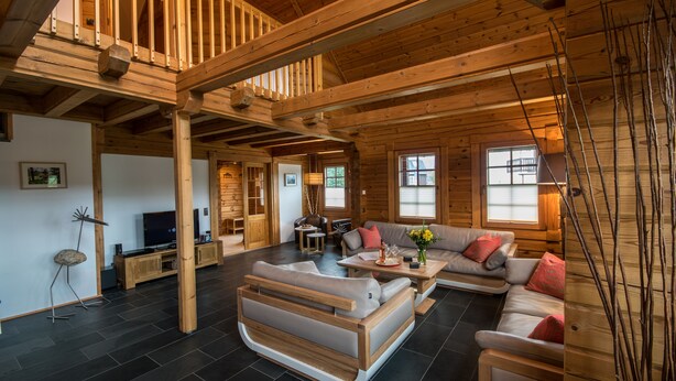A spacious living area with a high ceiling, wooden beams, a sofa set, a coffee table, and a TV. - Comfortable wooden house in the heart of Saxon Switzerland above Rathen (Bad Schandau OT Waltersdorf)