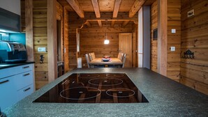 A modern kitchen with a central island, wooden walls, and a dining area with a table and chairs. - Comfortable wooden house in the heart of Saxon Switzerland above Rathen (Bad Schandau OT Waltersdorf)