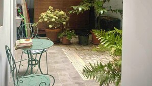 A small outdoor patio with a table and chairs, surrounded by potted plants and a brick wall.