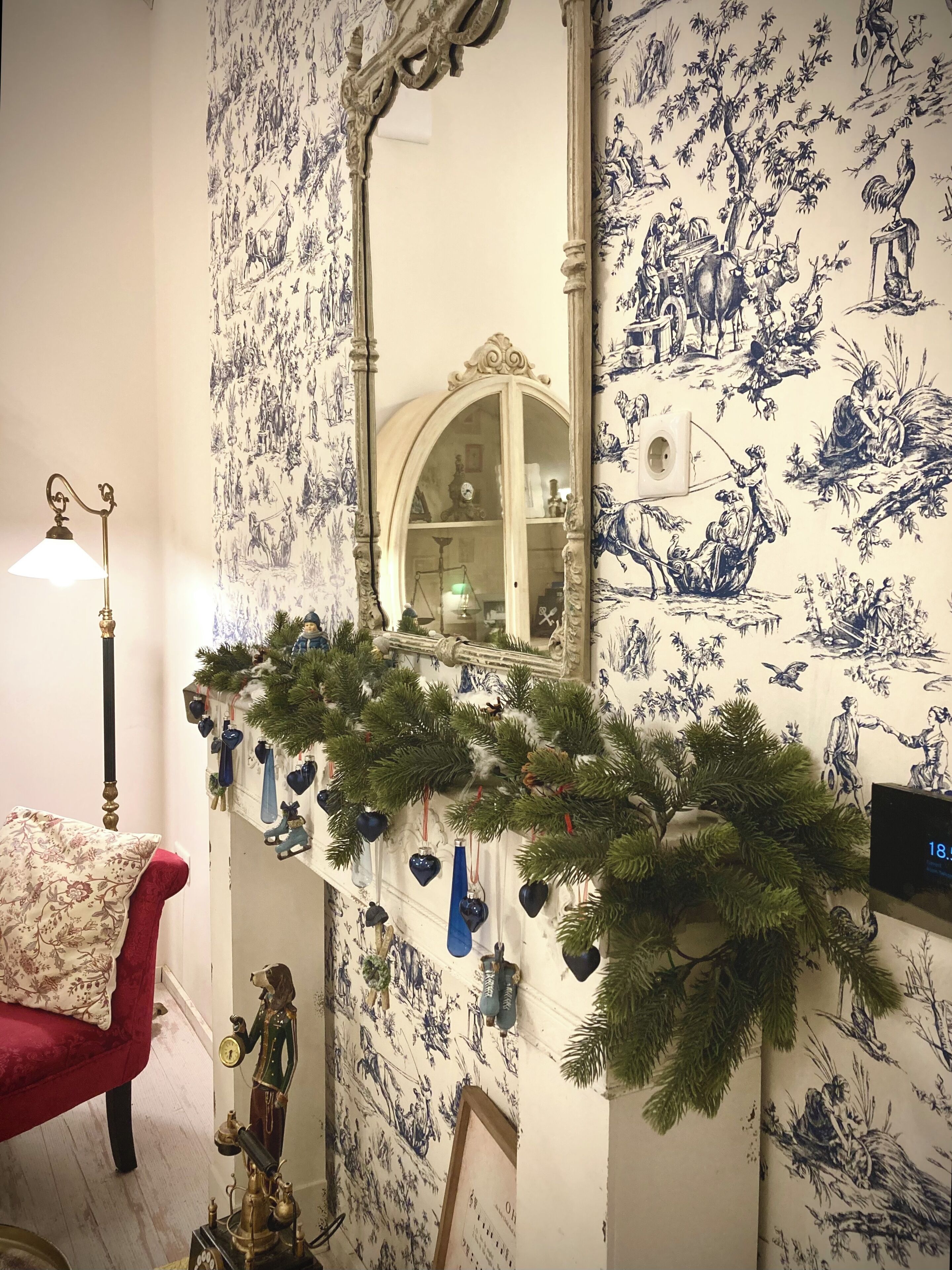 A room with a patterned wallpaper, a mirror, a red chair, and a Christmas garland.