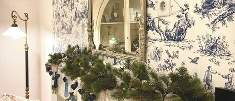 A room with a patterned wallpaper, a mirror, a red chair, and a Christmas garland.