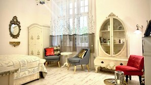 A room with a bed, a small round table, a red chair, a white wardrobe, and a large armoire with glass doors.