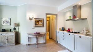 A modern kitchen with white cabinets, a gas stove, and a stainless steel range hood. There is a small table with a vase and a picture frame on the wall. - Monte - Independent House with private Pool, 4 People, Garden WiFi, A/C, Sicily (Ragalna)