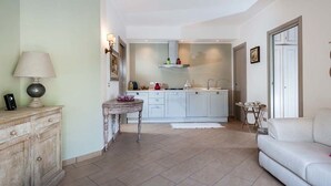 A spacious living area with a sofa, a small table, and a lamp. A kitchen with white cabinets and a tiled backsplash is visible in the background. - Monte - Independent House with private Pool, 4 People, Garden WiFi, A/C, Sicily (Ragalna)