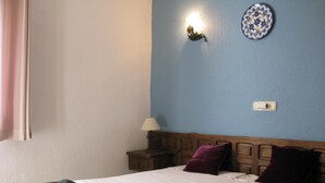 Een slaapkamer met een bed, nachtkastje, lamp, wandklok en decoratief bord.
