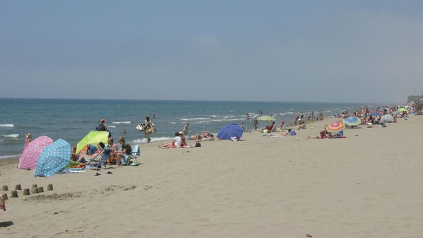Een strand met mensen die zonnebaden, parasols en een heldere lucht.