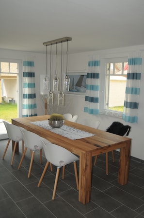 Un coin repas avec une table en bois, des chaises blanches, un cactus en guise de centre de table et un luminaire suspendu.