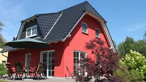 A red house with a black roof, a patio with chairs, and a tree with red leaves. - Schüßler house The red house - Schüßler (Trassenheide)
