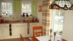 A kitchen with white cabinets, a wooden dining table, and a window with curtains. - Schüßler house The red house - Schüßler (Trassenheide)