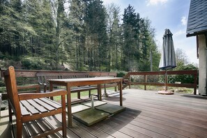 A wooden deck with a picnic table and benches, surrounded by a forested area.