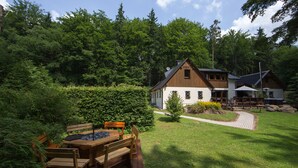 A wooden deck with a table and benches, surrounded by a well-maintained lawn and a hedge. - Ferienhaus Oppach (Oppach)
