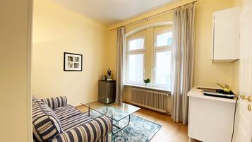 Ein Wohnzimmer mit einer Couch, einem Couchtisch, einem Heizkörper, einem Fenster mit Vorhängen und einem Schrank.