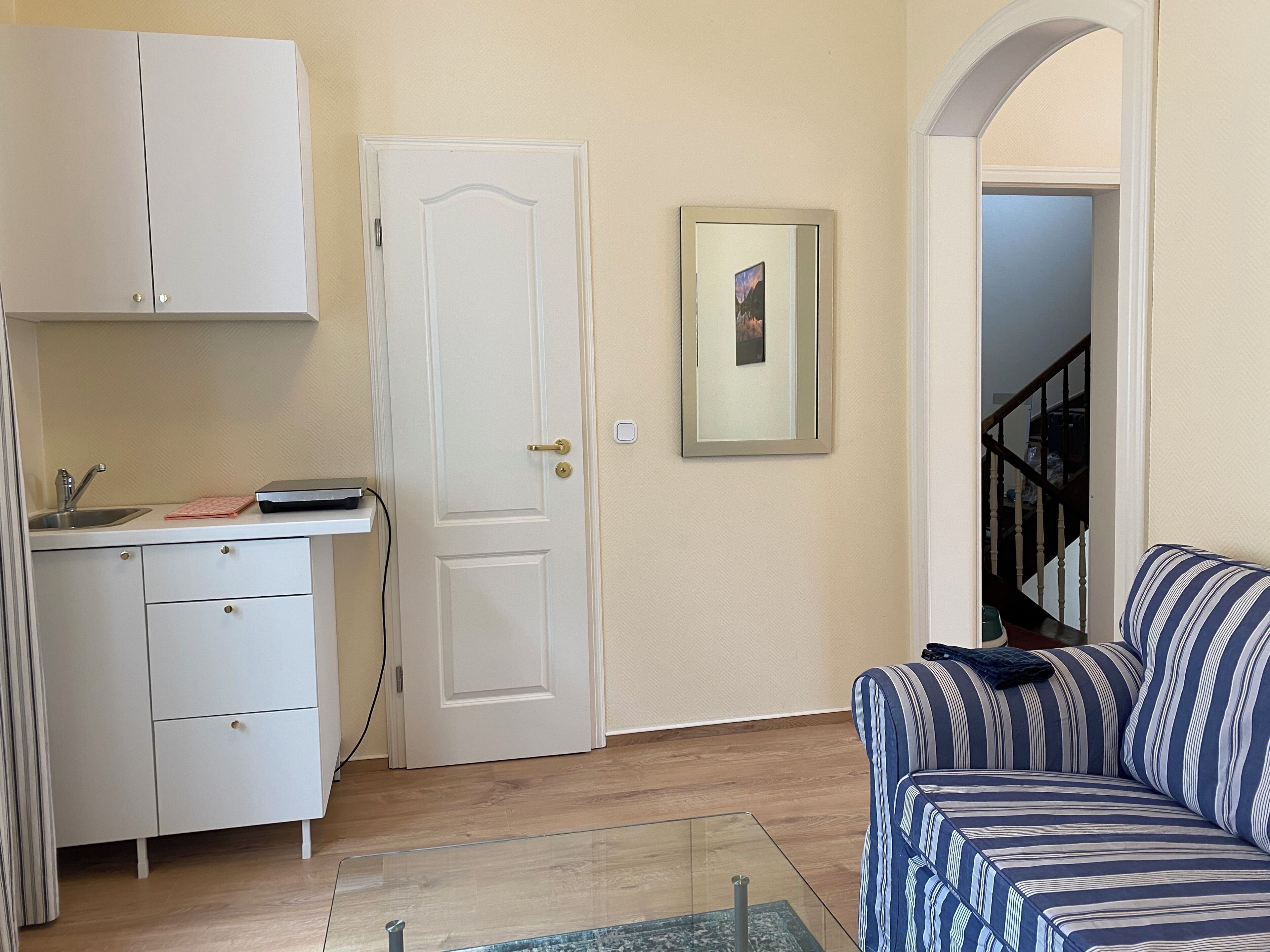 A compact living space with a kitchenette, a sofa, and a door leading to a staircase.