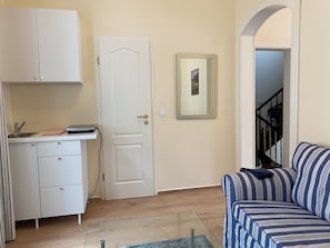 A compact living space with a kitchenette, a sofa, and a door leading to a staircase.