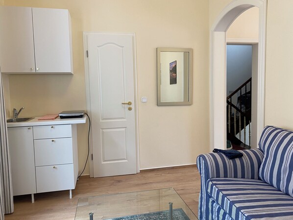 A compact living space with a kitchenette, a sofa, and a door leading to a staircase.