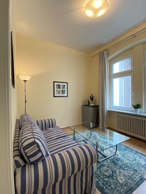 Un saló modern amb un sofà estriat, una taula de centre de vidre, una làmpada de peu, un radiador i una finestra amb cortines.
