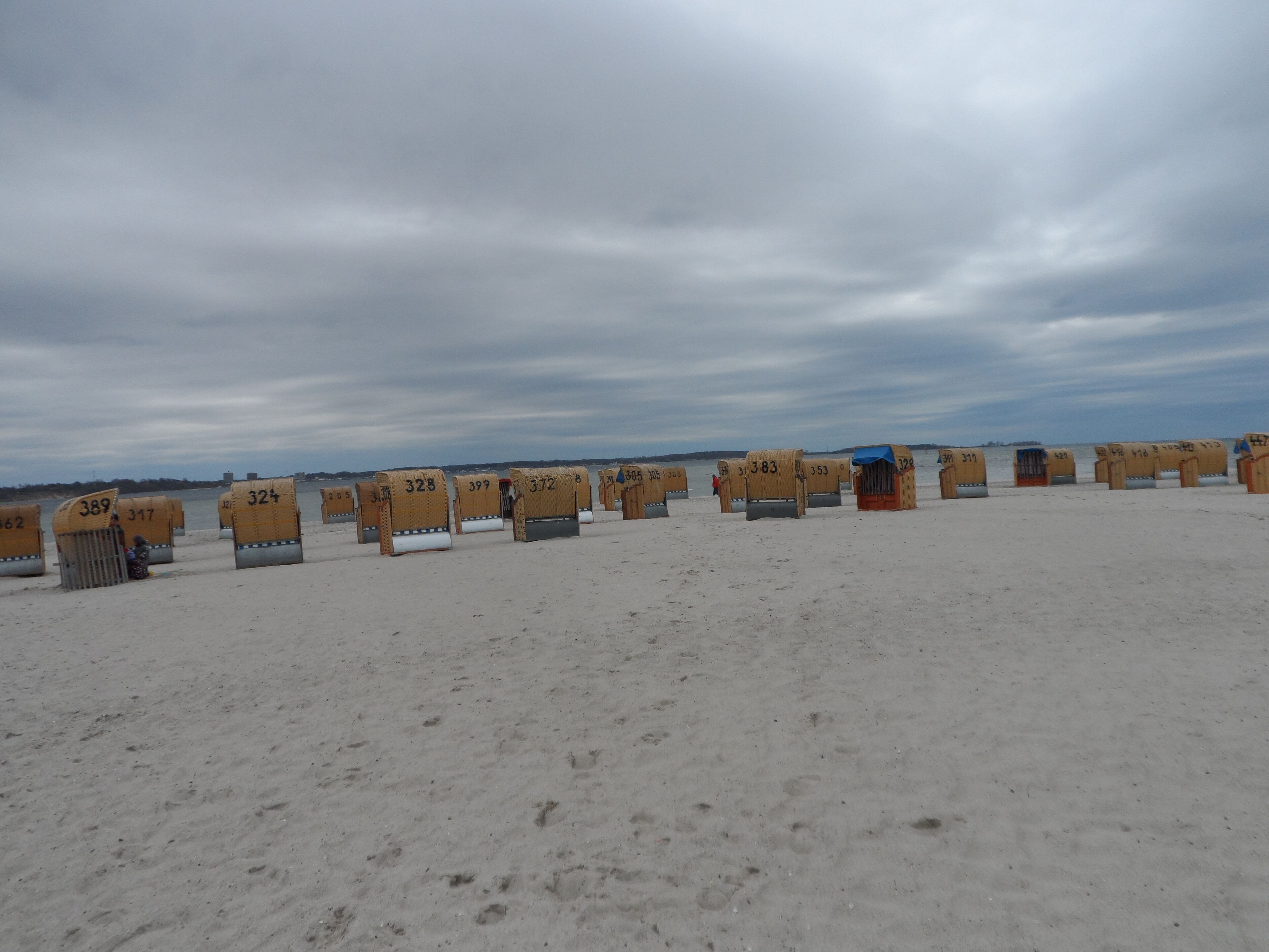 A row of numbered beach huts on a sandy beach with a cloudy sky.