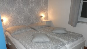 A neatly made bed with patterned bedding, a bedside lamp, and a window with curtains. - Ground floor apartment in apartment complex Fördeblick  (Laboe)