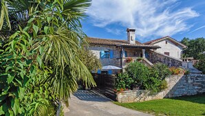 A stone house with a tiled roof, a paved driveway, and a stone wall with a flower bed. - Erisa in Trošti (Haus für 6 Personen) (Pazin)