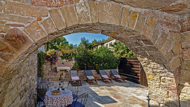 An outdoor patio with stone walls, a table with a floral tablecloth, and sun loungers. - Erisa in Trošti (Haus für 6 Personen) (Pazin)