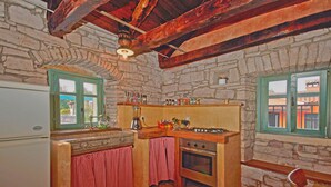 A rustic kitchen with stone walls, a wooden countertop, a built-in oven, and a window with green shutters. - Erisa in Trošti (Haus für 6 Personen) (Pazin)