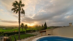 A swimming pool with a view of a sunset over a green landscape and palm trees. - Holiday house with pool in the heart of Mallorca (Sant Joan)
