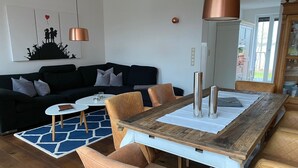 A modern living room with a dark-colored sofa, a round coffee table, and a wooden dining table with two chairs.