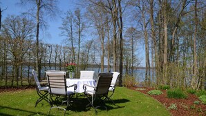 An outdoor seating area with a table and chairs, surrounded by a fence and trees, overlooking a body of water.