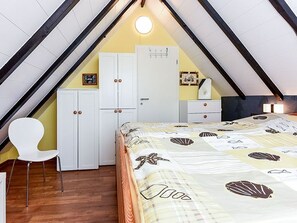 Een slaapkamer met een schuine kap, een bed met een beddegoed met dessin, een witte stoel en een kledingkast.