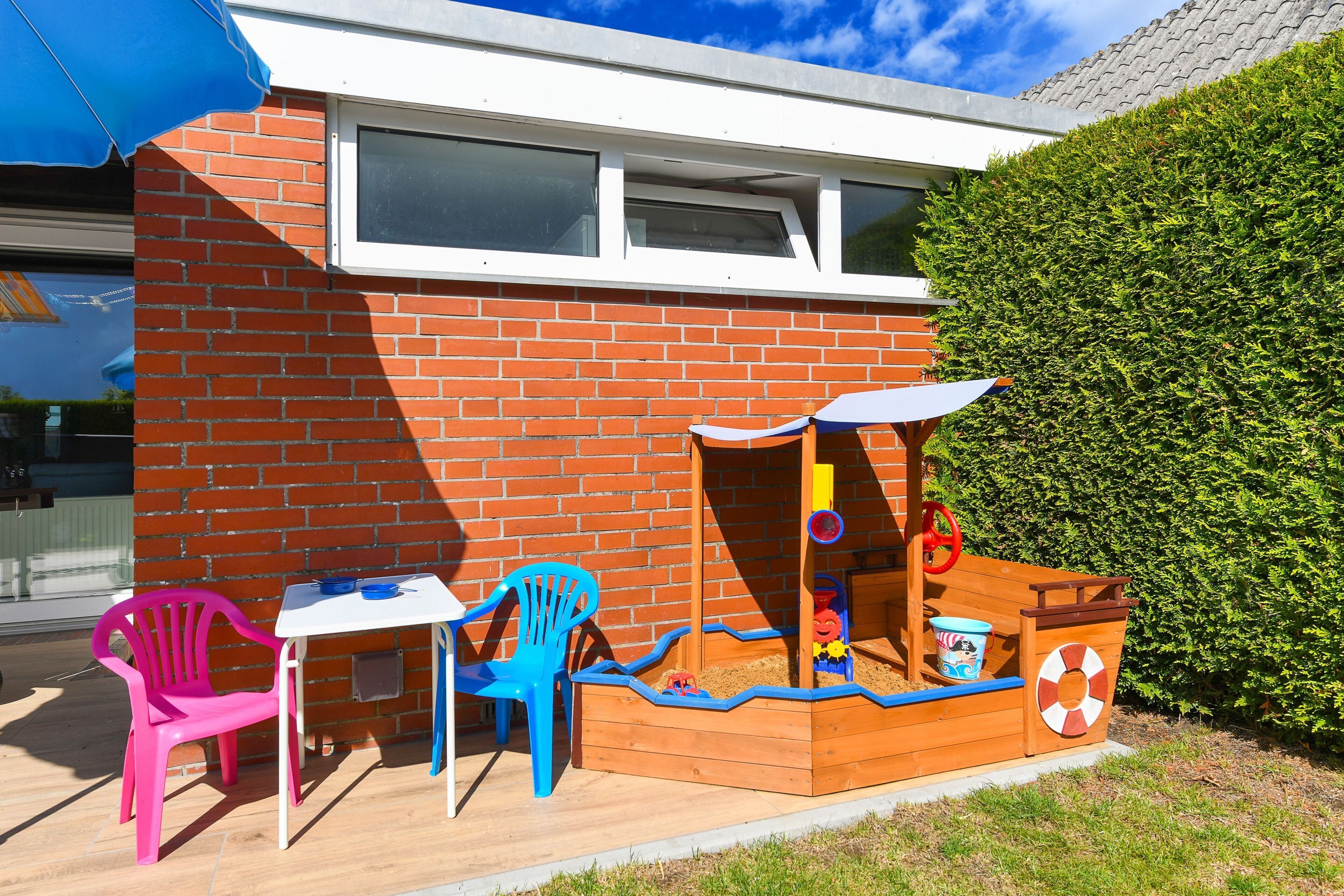 A wooden playhouse with a slide, a table with chairs, and a blue umbrella.