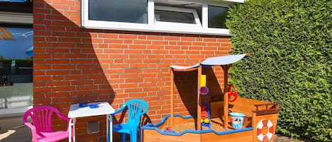 Una casita de juegos de madera con un tobogán, una mesa con sillas y un paraguas azul.