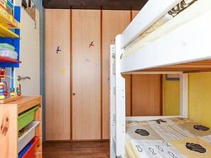 Ein Schlafraum mit Etagenbetten, einem Holzschrank, einem kleinen Holztisch mit Spielzeug und einem bunten Regalsystem.