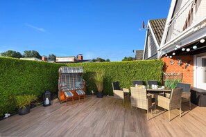 Eine Terrasse mit Gartenmöbeln, einer Hecke und einer Backsteinmauer.