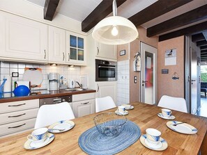 A modern kitchen with white cabinets, a wooden dining table, and a hanging light fixture.