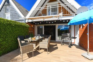 Eine Terrasse mit Gartenmöbeln, einem Grill und einem blauen Sonnenschirm.
