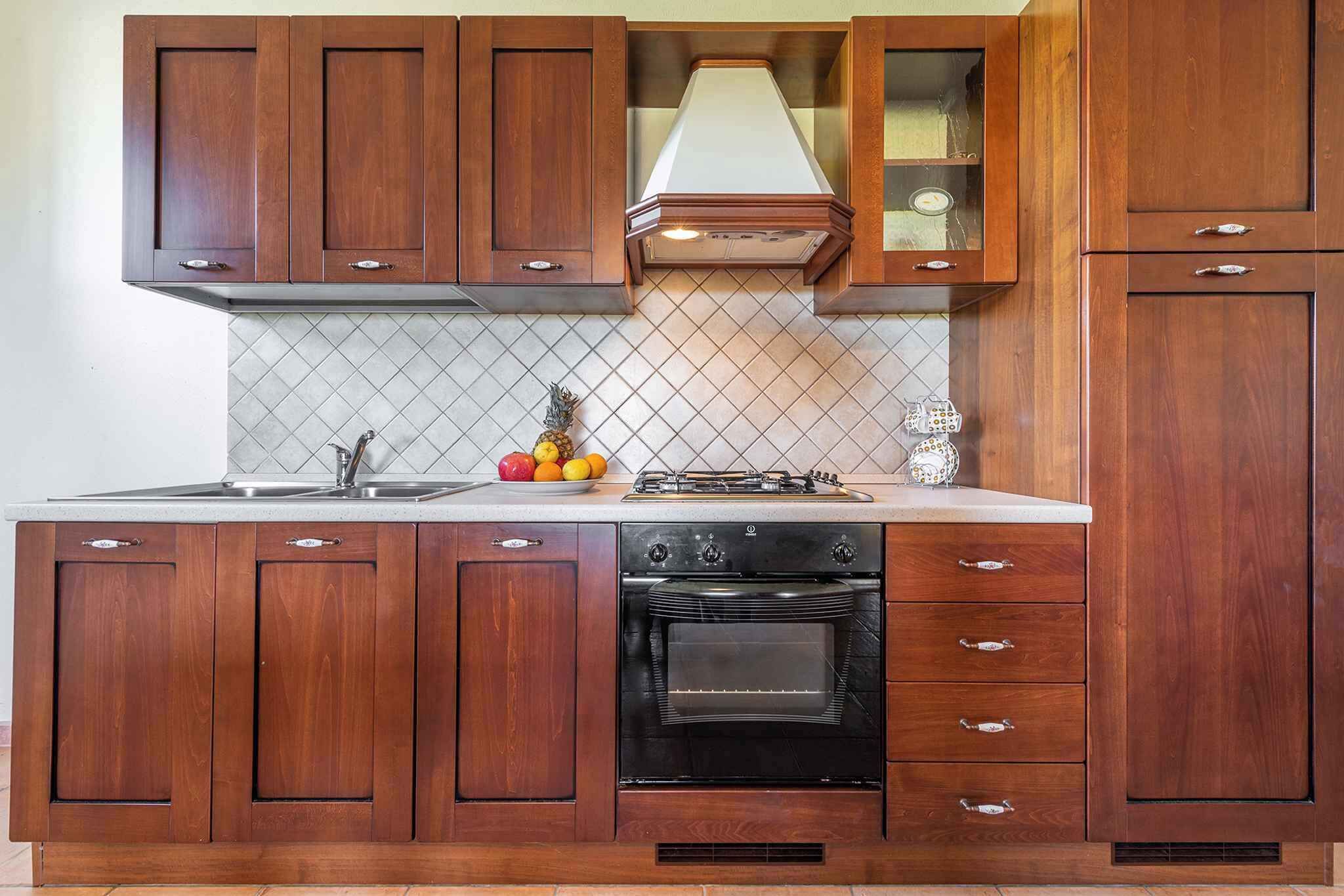 Eine Küche mit Holzausstattung, einer Edelstahl-Spüle, einem schwarzen Backofen und einer gefliesten Spritzschutzwand.