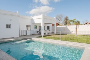 A modern house with a swimming pool, a covered patio, and a fenced backyard.
