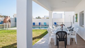 An outdoor dining area with a pool view, white walls, and blue chairs. - Holiday Home 'Villa Charco del Sultán' with Wi-Fi, Pool, Terrace & Garden (Conil de la Frontera)
