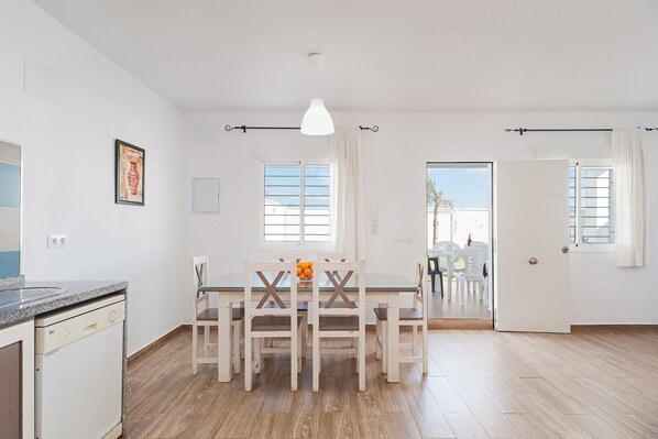 A dining area with a table and chairs, a pendant light, and a view through an open door.