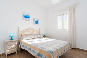 A bedroom with a bed, two bedside tables, a window with curtains, and two wall-mounted pictures.
