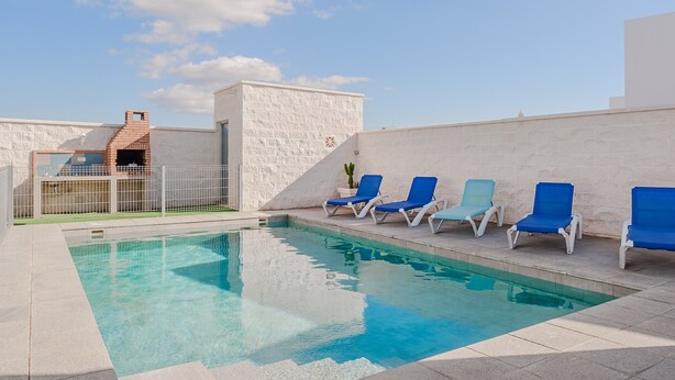 A rooftop pool with a clear blue pool, white stone walls, and blue lounge chairs. - Holiday Home 'Villa Charco del Sultán' with Wi-Fi, Pool, Terrace & Garden (Conil de la Frontera)