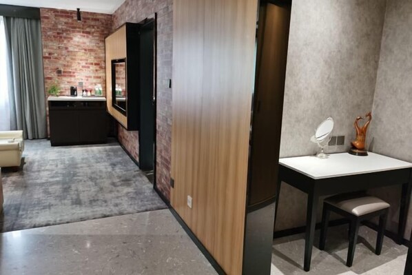 Habitación de hotel moderna con pared de ladrillo, puerta de madera, pequeña cocina americana, escritorio con silla y espejo.