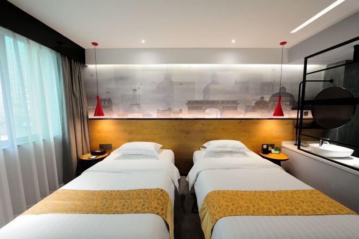 Habitación de hotel con dos camas, un ventanal con cortinas y vistas a un paisaje urbano, con un diseño moderno.