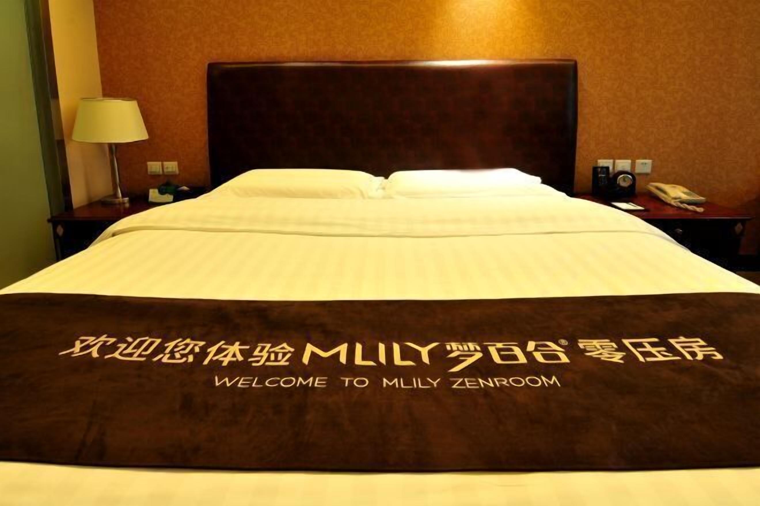 A hotel room with a large bed, a headboard, a nightstand with a lamp, and a phone.