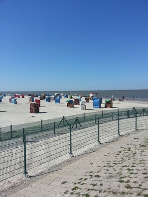 A beach with numerous colorful containers, a green fence, and a clear sky. - Vacation apartment on the North Sea / seawall, quiet central location, modern, Wi-Fi, sleeps up to 5 people (Nessmersiel)