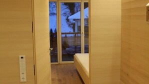 Un intérieur en bois comprenant un lit, une porte-fenêtre coulissante donnant sur un espace extérieur et un thermostat fixé au mur.