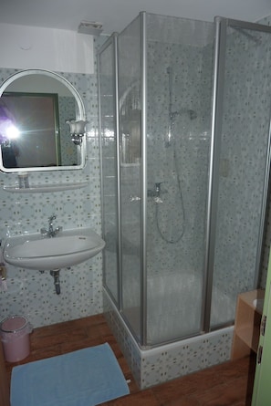 A bathroom with a glass-enclosed shower, a sink with a mirror above it, and patterned tiles on the walls.