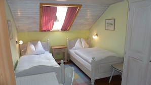 A bedroom with two beds, a small table, a nightstand, a window with curtains, and a door. - Heissbauer Vacation Rental "Karwendelblick" with Mountain Views, 2 Bedrooms, and 2 Bathrooms (Wackersberg)