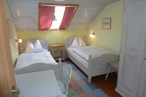 A bedroom with two beds, a small table, a nightstand, a window with curtains, and a door.