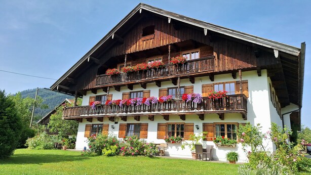 A multi-story building with balconies adorned with flower boxes, a white facade, and wooden balconies. - Heissbauer Vacation Rental "Karwendelblick" with Mountain Views, 2 Bedrooms, and 2 Bathrooms (Wackersberg)